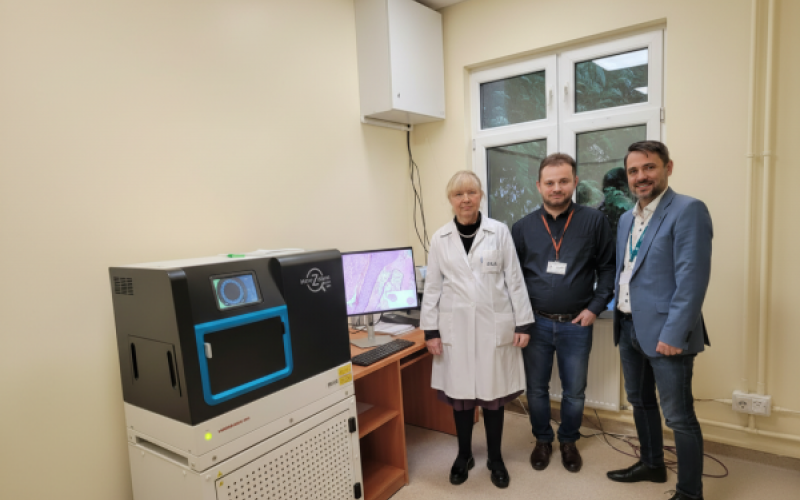 skaner, w tle Kierownik Pracowni Patomorfologii dr Jadwiga Sierocińska - Sawa, Z-ca dyr. ds. Informatyzacji Mariusz Musiatowicz, w środku przedstawiciel firmy wdrażającej system (fot. A.Guzowska 11.12.25)